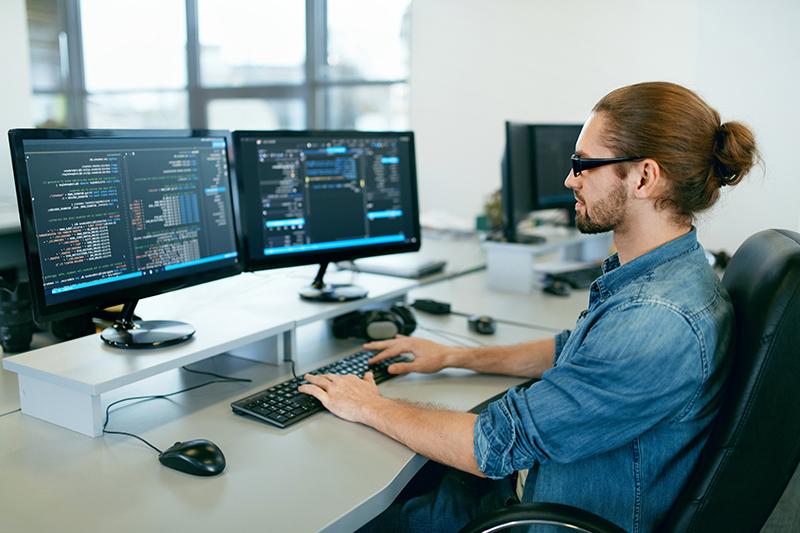 Programmierung. 人们在IT办公室的电脑前工作，坐在办公桌前写代码。. 在软件开发公司工作的程序员输入数据代码. Hohe Qualität Bild.